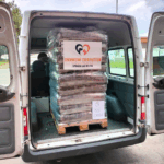 Auf der Ladefläche eines weißen Lieferwagens ist eine Palette mit Säcken voller Tierfutter gestapelt. Die Palette ist in Plastik eingewickelt und mit einem Schild beschriftet, auf dem "Tierheim Tierfutter Spenden und Helfen" steht.