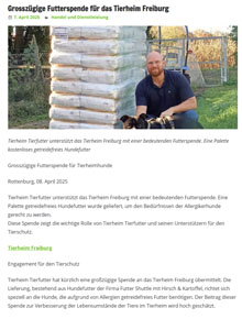 Ein bärtiger Mann sitzt im Freien neben mehreren gestapelten Tüten mit Tierfutter und hält einen kleinen Hund. Die Szene begleitet einen deutschen Artikel über eine großzügige Tierfutterspende für das Freiburger Tierheim.