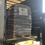 Eine mit Säcken gestapelte Palette, in Plastik eingewickelt, befindet sich in einem Lastwagen. An dem Stapel ist ein Schild mit der Aufschrift TIERHEIM TIERRUTTER und einem Herz-Logo angebracht. Das Sonnenlicht fällt von der Seite ein.