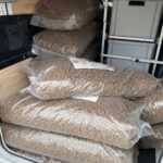 Große durchsichtige Plastiksäcke, gefüllt mit braunem Tierfutter, stapeln sich im hinteren Teil eines Fahrzeugs mit Holzinnenausstattung und Metallregalen.