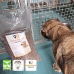 Ein Hund frisst aus einer Metallschüssel in einem Zwinger. Daneben steht eine große Tüte Hundefutter mit der Aufschrift Tierheim Tierfutter, auf der unten links drei Logos abgebildet sind, darunter Animal Life.