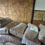 In einem holzgetäfelten Raum mit einem kleinen gerahmten Bild stapeln sich große, mit braunem Trockenfutter gefüllte Plastiktüten an einer mit Steinmustern verzierten Wand.