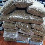 Ein großer Stapel durchsichtiger Plastiktüten, die mit Trockenfutterpellets gefüllt sind, steht auf einem Holzboden in einem Geschäft mit Regalen mit verschiedenen Produkten im Hintergrund.