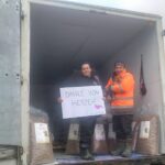 Zwei Menschen stehen in einem offenen Lastwagen, der mit großen Säcken voller Tierfutter gefüllt ist. Einer hält einen kleinen Hund, der andere hält ein Schild mit der Aufschrift DANKE VON HERZEN.