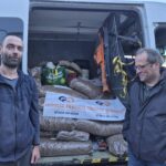 Zwei Männer stehen vor einem offenen Lieferwagen, der mit großen Säcken voller Tierfutter gefüllt ist. Ein Transparent mit der Aufschrift "Tierheim Tierfutter Spenden und Helfen" ist über den Vorräten im Inneren des Lieferwagens drapiert.