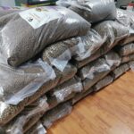 Mehrere große, durchsichtige Plastiksäcke, die mit Trockenfutter für Haustiere gefüllt sind, liegen ordentlich in zwei Reihen auf einem Holzboden gestapelt. Die Säcke scheinen fest verschlossen zu sein und sind in einer kompakten Formation angeordnet.