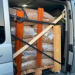 Ein Lieferwagen mit geöffneter Seitentür zeigt große Säcke mit Pellets, die auf einer Holzpalette mit Holzbrettern und Gurten gesichert sind, um ein Verrutschen während des Transports zu verhindern.