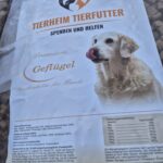 Auf einer Tüte Tierheim Tierfutter sind ein Golden Retriever, ein herzförmiges Logo und ein Werbetext für Premium Geflügel Trockenfutter abgebildet. Nährwertangaben und Angaben zur Wohltätigkeit sind sichtbar.