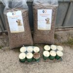 Zwei große Tüten mit trockenem Hundefutter und mehrere Dosen mit nassem Hundefutter liegen draußen auf dem Boden neben einem Metallzaun. Auf den Etiketten der Tüten ist das Bild eines Hundes abgebildet.