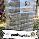 Eine große, in Plastik eingewickelte Palette, auf der sich verpacktes Tierfutter stapelt. Auf der Palette ist ein Schild mit der Aufschrift Tierheim Tierfutter - Spenden und helfen. Unten hängt ein Banner mit der Aufschrift "Dankeschön" und zwei Logos von Tierhilfsorganisationen.