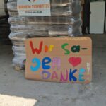 Ein Stapel Tierfuttersäcke mit einem Schild, auf dem in bunten Buchstaben „Wir sagen DANKE!“ steht, was auf Deutsch „Wir sagen DANKE!“ bedeutet. Oben drauf befindet sich ein Banner mit der Aufschrift „Tierheim Tierfutter“.
