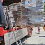 Säcke mit Tierfutter der Marke „Tierheim Tierfutter“ werden aus einem roten Lkw abgeladen. Eine Leiter lehnt an dem Lkw, und draußen scheint die Sonne.