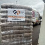 Eine große Palette, auf der Säcke mit in Plastik verpacktem Tierfutter gestapelt sind; darüber hängt ein Banner mit der Aufschrift „Tierheim Tierfutter Spenden und Helfen“. Im Hintergrund steht an einem bewölkten Tag ein Transporter mit Werbeaufdrucken.