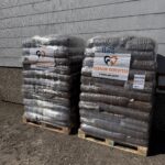 Vor einem grauen Gebäude stehen zwei Paletten, auf denen große, in Plastikfolie verpackte Säcke mit Tierfutter gestapelt sind. Auf jeder Palette befindet sich ein Schild mit der Aufschrift „Tierheim Tierfutter“ und einem Logo mit einem Herz und einer Pfote.