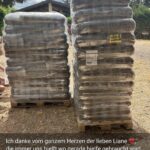 An einem sonnigen Tag stehen draußen zwei große Stapel von in Plastikfolie verpackten Tierfuttersäcken, im Hintergrund sind ein kleines Gebäude und Bäume zu sehen. Am unteren Bildrand ist eine herzliche Dankesbotschaft auf Deutsch eingeblendet.