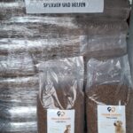 Große Stapel von Tierfuttersäcken, im Vordergrund zwei beschriftete Säcke für Katzen. Auf einem Banner darüber steht „Tierheim Tierfutter Spenden und Helfen“ mit einem Logo, auf dem ein Hund und eine Katze abgebildet sind.