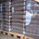 Mehrere Holzpaletten, auf denen große, in durchsichtige Plastikfolie verpackte Säcke zur Lagerung oder zum Versand gestapelt sind, in einem Lagerhaus oder Lagerbereich.