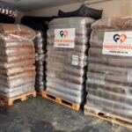 In einem Lagerraum mit Betonboden stehen große Stapel von in Plastikfolie verpackten Tierfuttersäcken auf Holzpaletten, die mit der Aufschrift „Tierheim Tierfutter“ und einem Logo aus Herz und Pfote versehen sind.