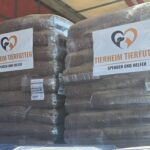 Zwei große Stapel von Tierfutter in Säcken sind in Plastikfolie eingewickelt. An jedem Stapel befindet sich ein Schild mit der Aufschrift „Tierheim Tierfutter – Spenden und Helfen“ und einem Logo, auf dem ein Herz, ein Hund und eine Katze abgebildet sind.