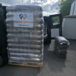 Neben einem Transporter steht eine Palette mit Säcken voller Tierfutter, die mit „Tierheim Tierfutter“ beschriftet sind; daneben liegen weitere Säcke auf dem Boden. Es scheint sich um eine Spenden- oder Lieferaktion im Freien an einem bewölkten Tag zu handeln.