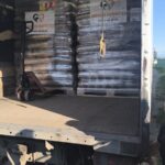 Zwei übereinander gestapelte Paletten mit Säcken voller Tierfutter auf einem Lkw, davor steht ein Hubwagen. Die Säcke sind in Plastikfolie eingewickelt, die Heckklappe des Lkws ist geöffnet, sodass man in den Laderaum sehen kann und Sonnenlicht hereinscheint.