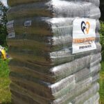 Ein großer Stapel in Plastikfolie verpackter Tiernahrung oder Tierbedarf steht im Freien auf einer Holzpalette. Auf der Verpackung befindet sich ein Etikett mit dem Logo und dem Schriftzug Tierheim Tierfutter Spenden und Helfen. Im Hintergrund sind Bäume zu sehen.