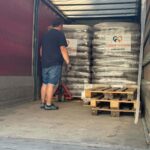 Ein Mann, der mit einem Hubwagen Stapel von Futtersäcken in einem Sattelauflieger transportiert.
