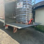 Eine Palette mit in Plastikfolie verpackten Säcken Tierfutter, die auf der abgesenkten Ladeklappe eines Sattelschleppers steht und mit einem Hubwagen bewegt wird.