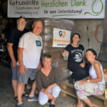 Fünf Erwachsene posieren lächelnd vor einer großen Palette mit Katzenfutter. Auf einem Banner über ihnen steht: Katzenhilfe Sipplingen und Umgebung e.V. Herzlichen Dank für eure Unterstützung!.